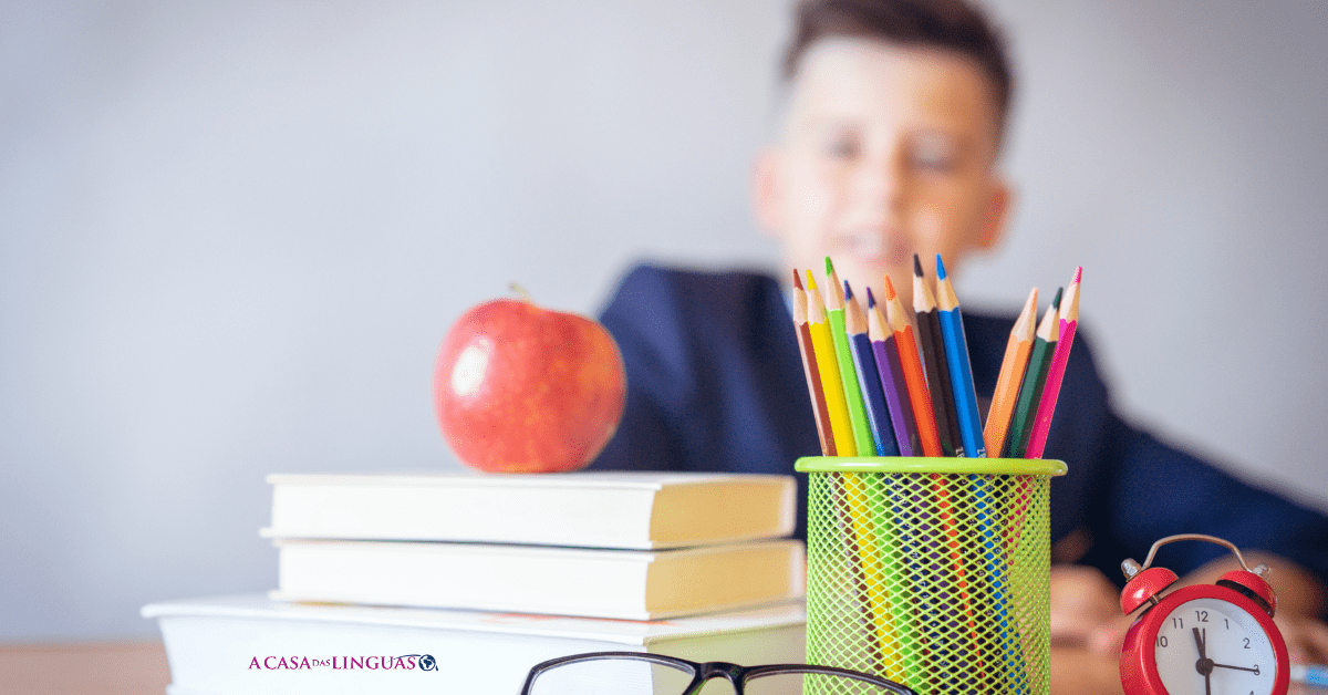 Manzana, libros y lápices de colores en primer plano y detrás un niño difuminado